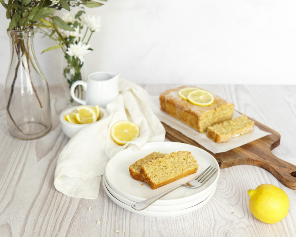 A sliced, Low FODMAP Lemon Loaf with Collagen and a lemon glaze, garnished with lemon.
