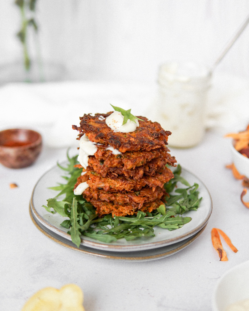 A pile of Low FODMAP sweet potato fritters with a drizzle of lemon aioli.
