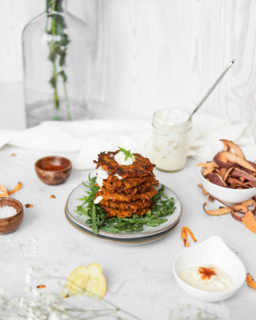 A pile of Low FODMAP sweet potato fritters with a drizzle of lemon aioli.