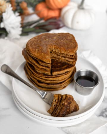 A stack of Low FODMAP & Paleo Pumpkin Pancakes with a slice ready to be eaten.