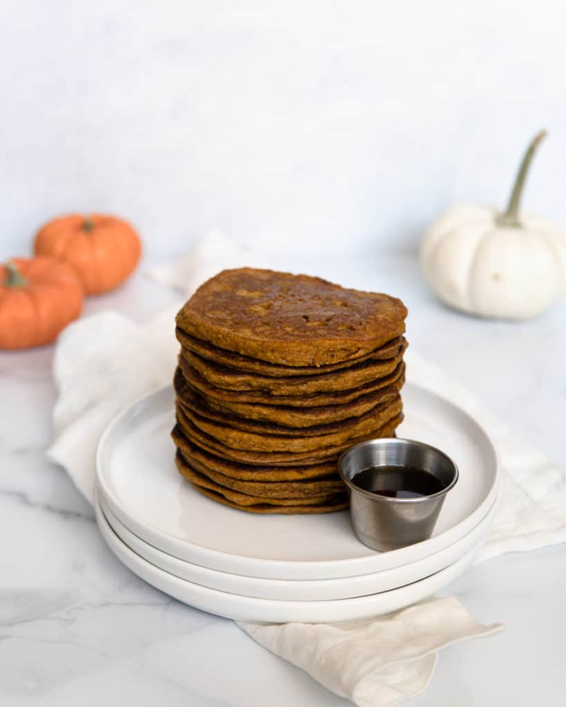 A stack of Low FODMAP & Paleo Pumpkin Pancakes with a side of maple syrup.