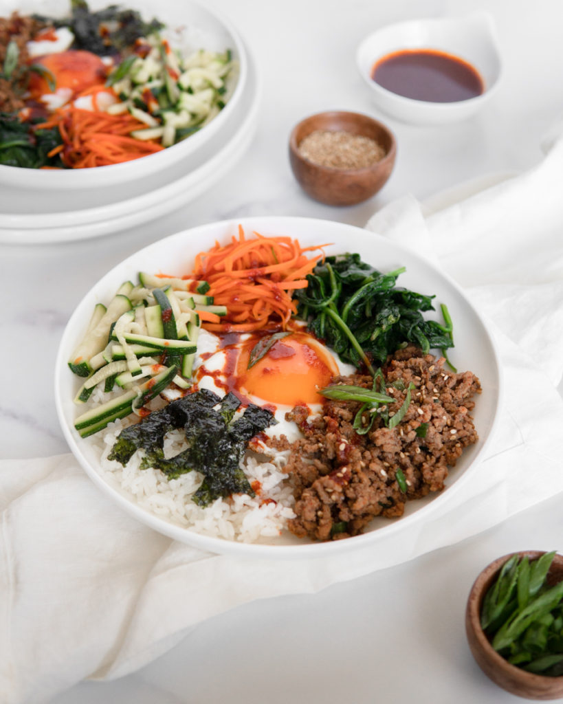 Easy Low FODMAP Bibimbap with Ground Beef and sauteed zucchini, carrot & spinach, topped with a fried egg, and a Low FODMAP sauce, served over rice.