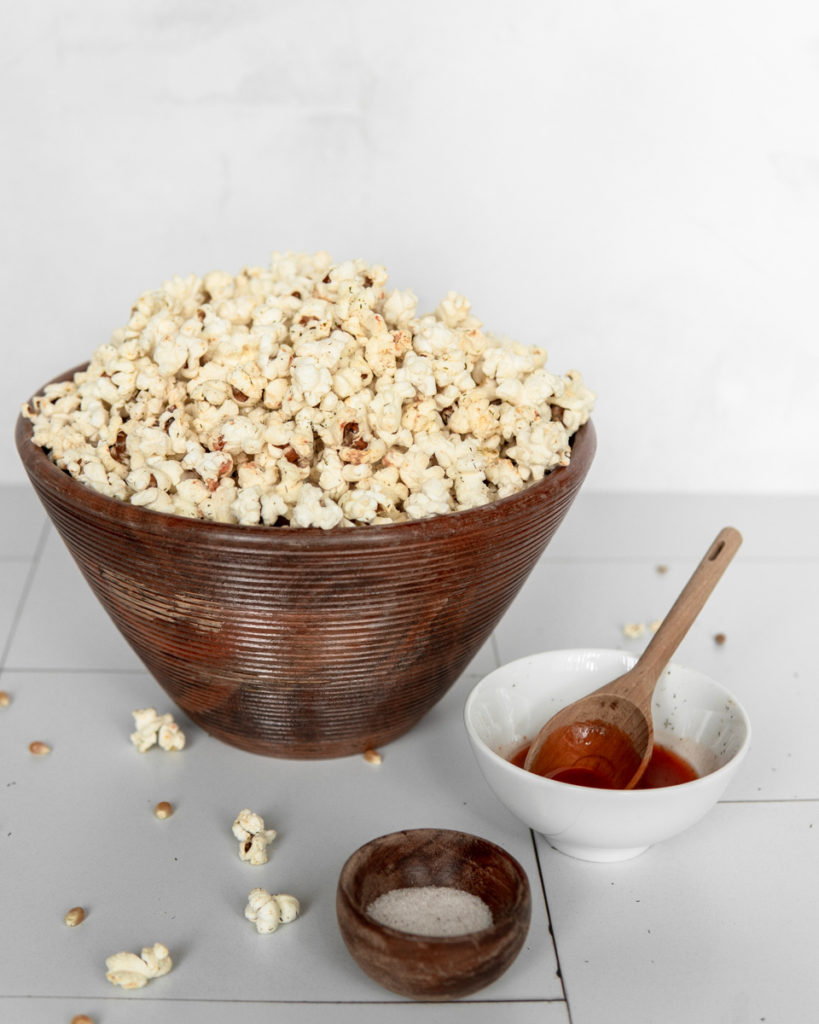 A large bowl of Low FODMAP Buffalo Ranch Popcorn, with a small side of hot sauce and fine sea salt for decoration.
