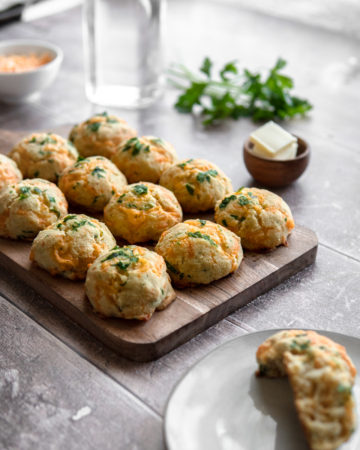 A tray of Low FODMAP cheddar buns, topped with parsley, with a side of butter.