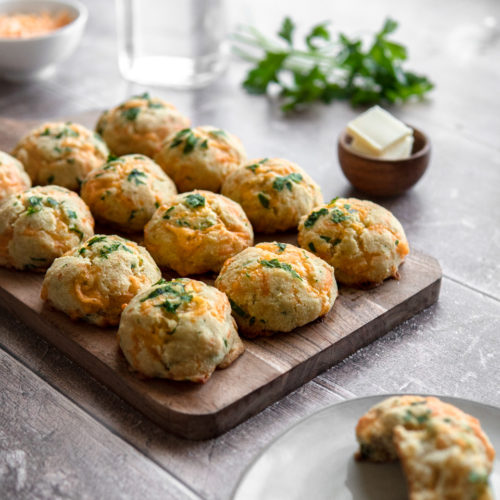 A tray of Low FODMAP cheddar buns, topped with parsley, with a side of butter.