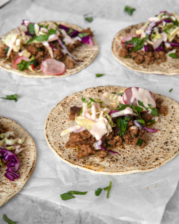 Low FODMAP ground beef bugolgi tacos laying flat, topped with quick pickled cabbage and sriracha mayo.