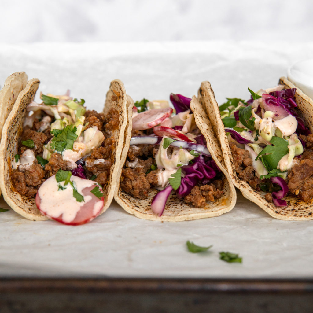 A row of Low FODMAP ground beef bugolgi tacos, topped with quick pickled cabbage and sriracha mayo.