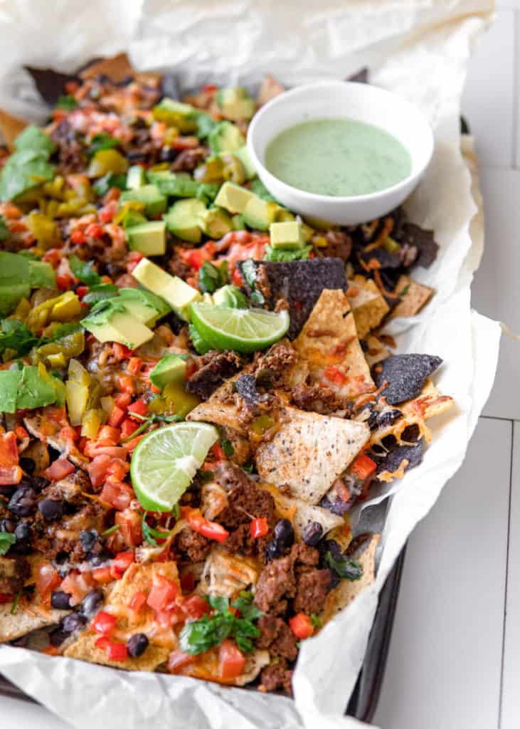 A platter of delicious Low FODMAP, loaded ground beef nachos garnished with lime and a side of jalapeno yogurt.