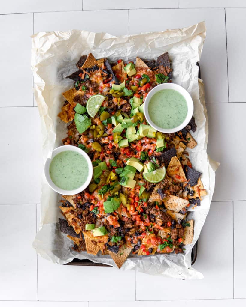 A platter of delicious Low FODMAP, loaded ground beef nachos garnished with lime and a side of jalapeno yogurt.