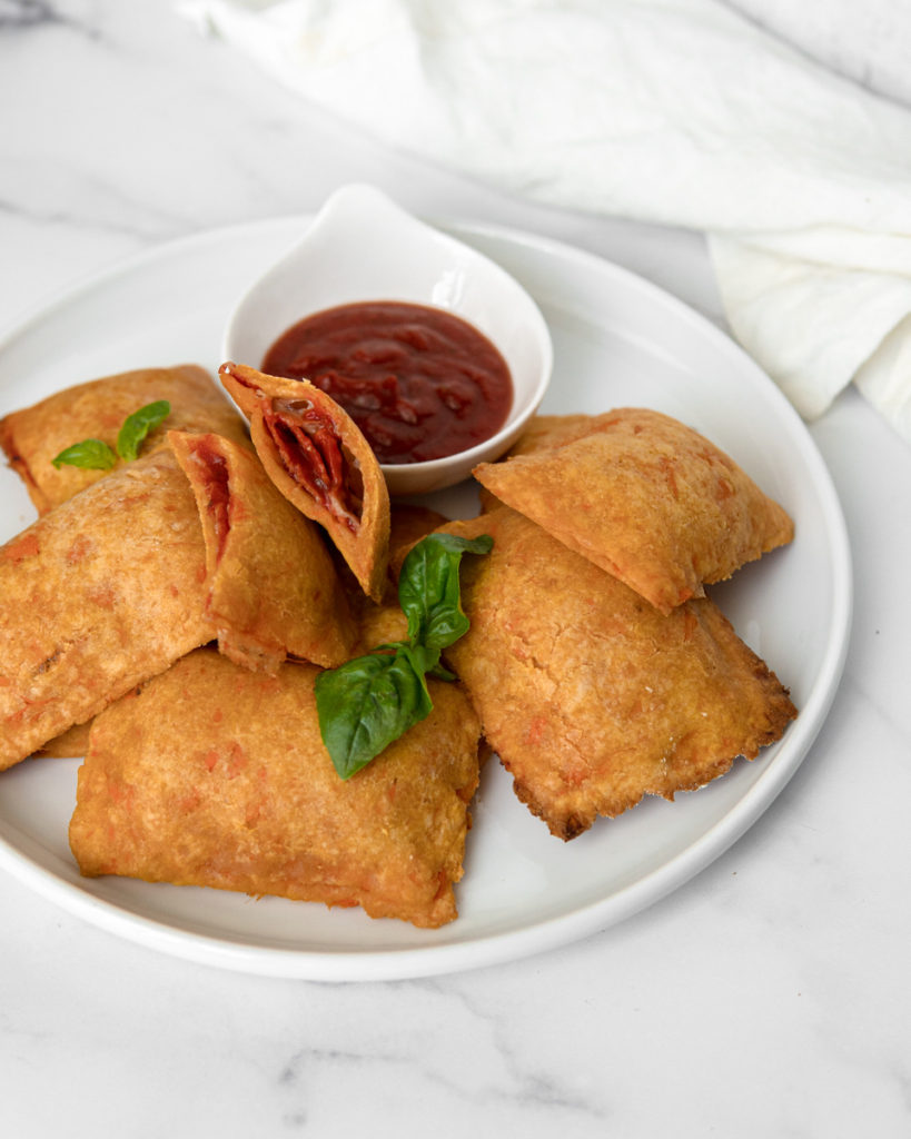 A plate of Low FODMAP & Grain Free homemade pizza roll filled with passata, pepperoni and mozzarella, cut open to show the hot and saucy insides. Served with a side of passata dipping sauce.